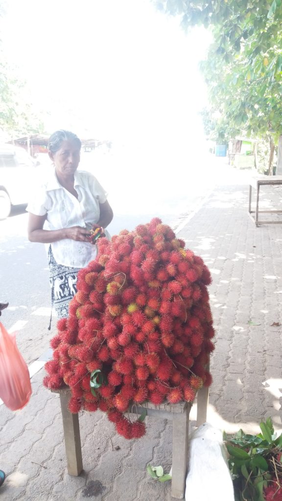 Prodejkyně rambutanu na ulici. Rambutan je červené chlupaté ovoce, které chutná jako liči.